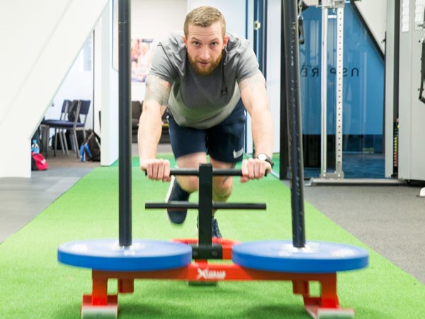 male pushing a sled during a hiit training session